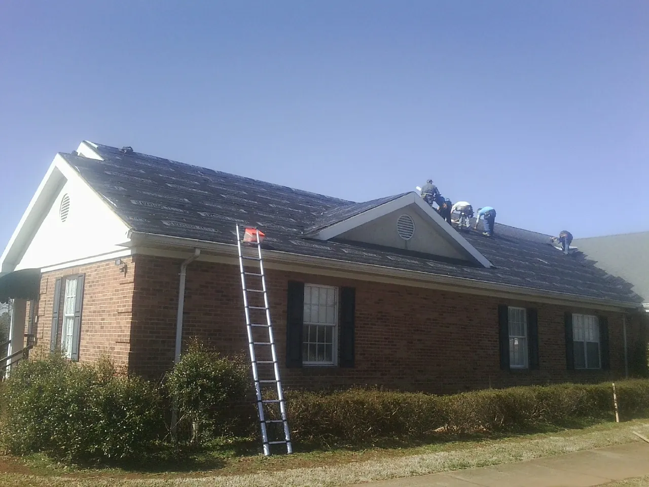 Crew tearing shingles off a brick ranch roof with a ladder set — Emergency Roof Repair work by our crew in Prior Lake