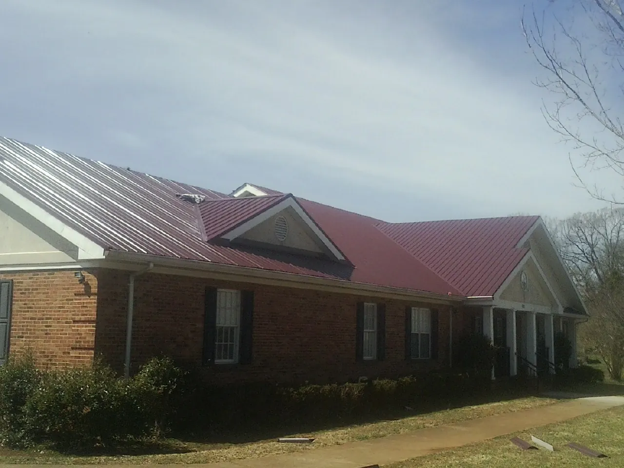 Red metal roof with gabled entries on a long brick building, from a Hail Damage Roof Repair job in Prior Lake