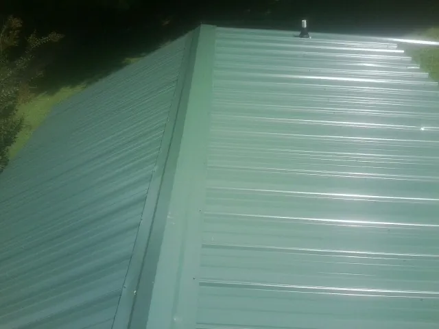New green metal panels meeting at the ridge of a roof — Flat Roof Repair work by our crew in Prior Lake