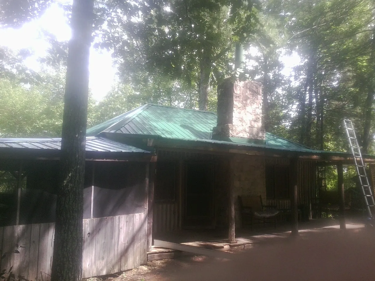 Green metal roof and stone chimney above a log cabin porch in Prior Lake