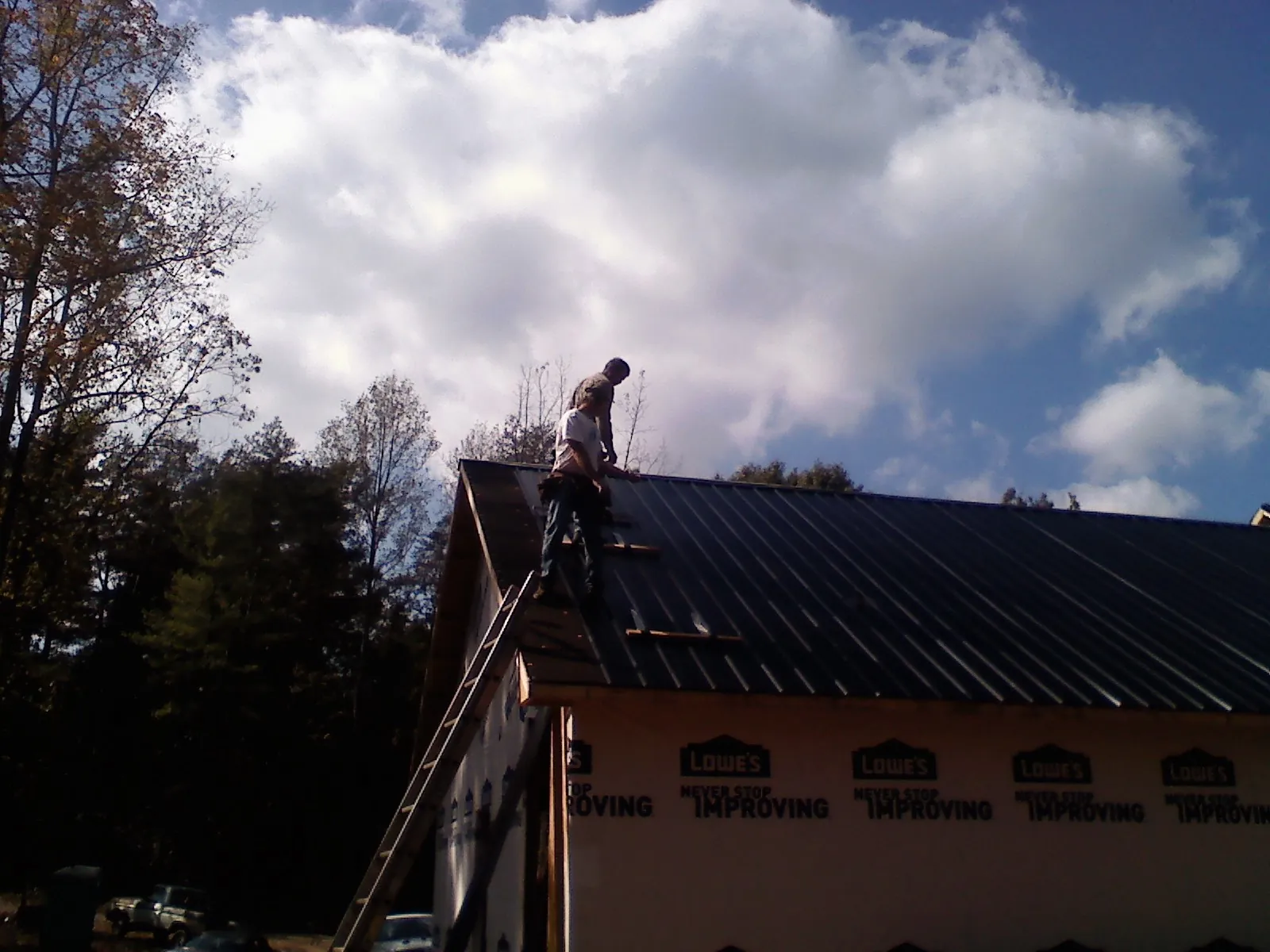 Roofer fastening dark metal panels high against a cloudy sky, from a Roof Inspection job in Prior Lake
