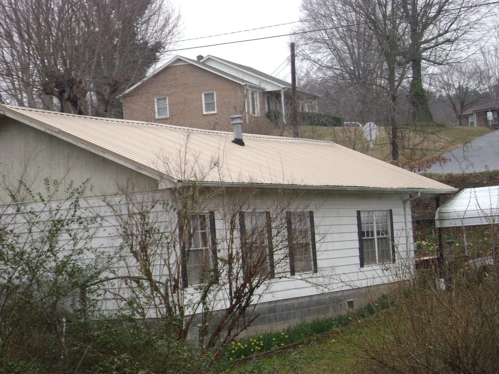 Tan metal roof on a white sided house set into a hillside — Commercial Roofing by Roofing Brothers in Prior Lake